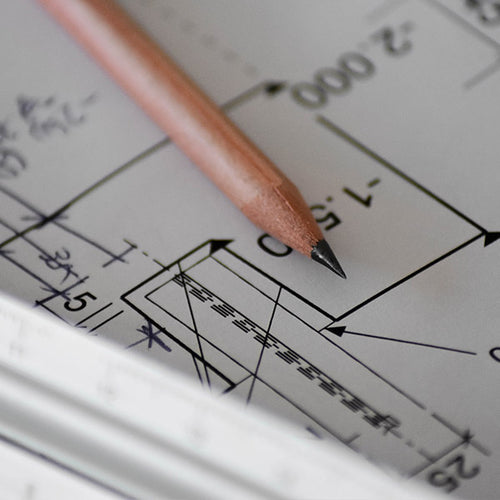 Pencil resting on detailed architectural blueprint with measurements.
